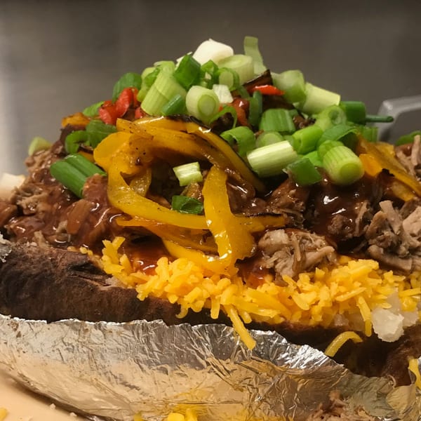 Baked potato topped with pulled pork, cheese, peppers, and green onions, served in foil.