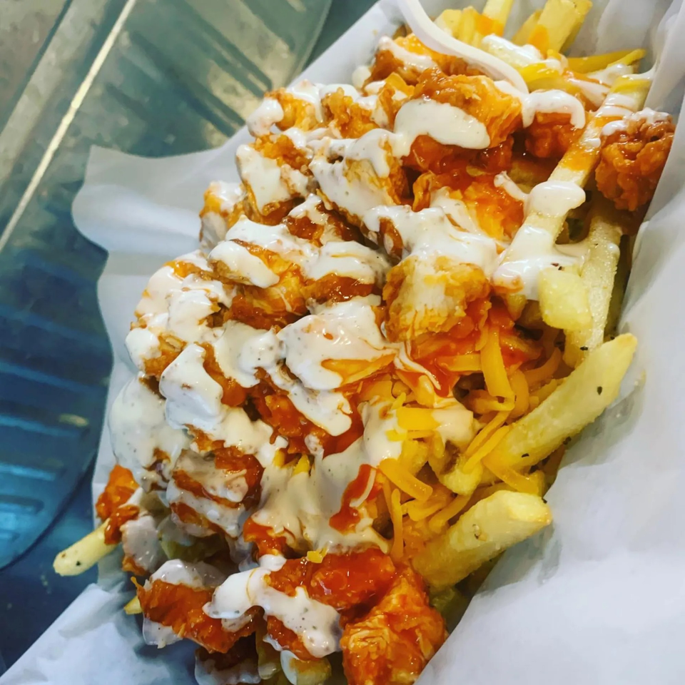 Buffalo chicken and cheese fries drizzled with ranch dressing, served in a white paper-lined basket.