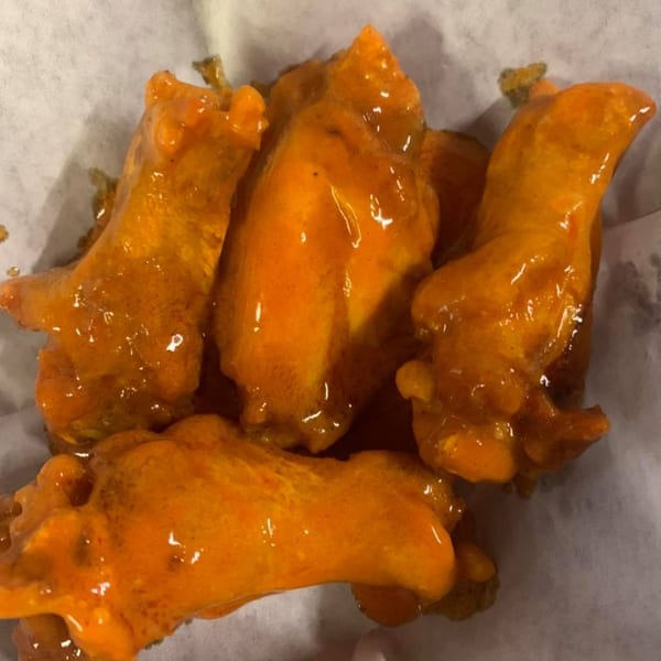 Four orange-glazed chicken wings, likely buffalo, resting on white parchment paper.