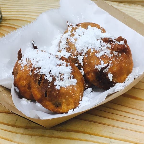 Four golden-brown fried hushpuppies, generously dusted with powdered sugar, in a paper-lined basket.