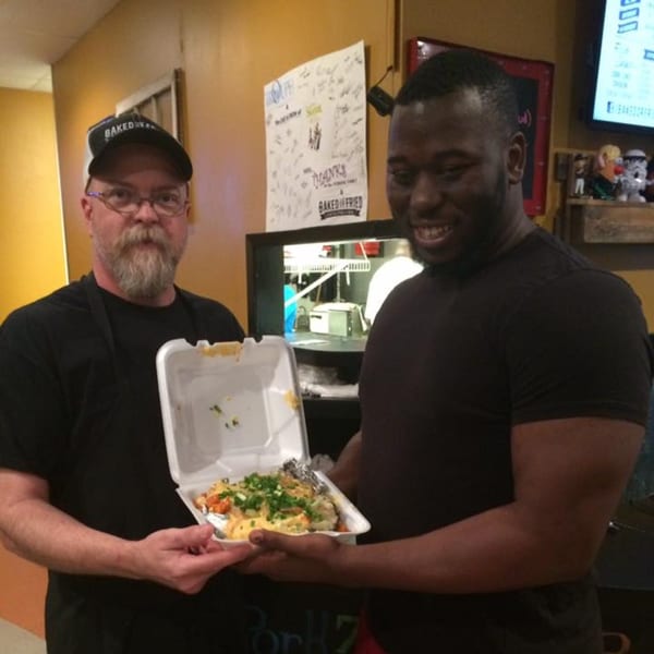 Two men, one bearded, holding a takeout container of southern food with mac and cheese.