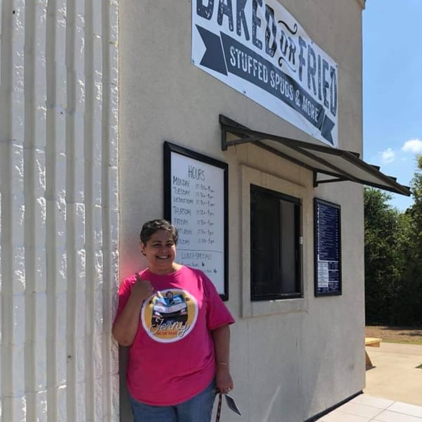 A woman in a pink shirt smiles outside the Baked or Fried restaurant building.